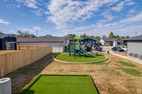 A playground with a green slide and a roundabout in the middle of a grassy area.
