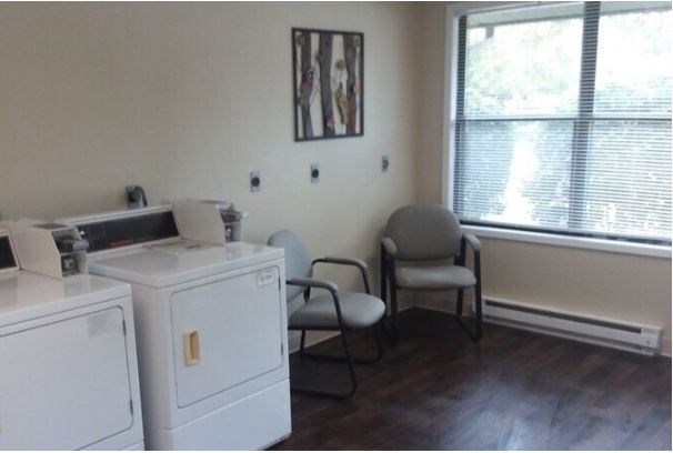 A laundry room with a washer and dryer, a chair, and a window.