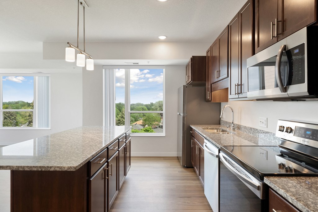 A kitchen with brown cabinets and a view of the outdoors through a sliding glass door at Sonder Point 50+ Apartments, Minnesota, 55430