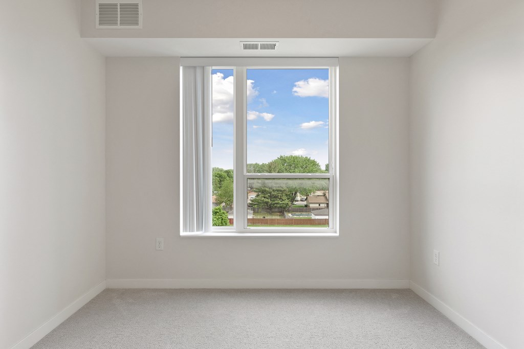 A room with a window showing a view of a residential area at Sonder Point 50+ Apartments, Brooklyn Center, MN, 55430
