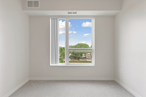 A room with a window showing a view of a residential area at Sonder Point 50+ Apartments, Brooklyn Center, MN, 55430