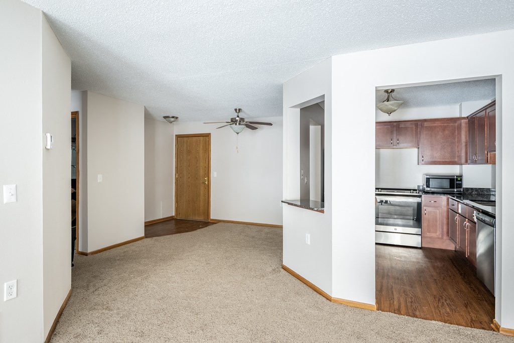 a living room with a ceiling fan and a kitchen in the background