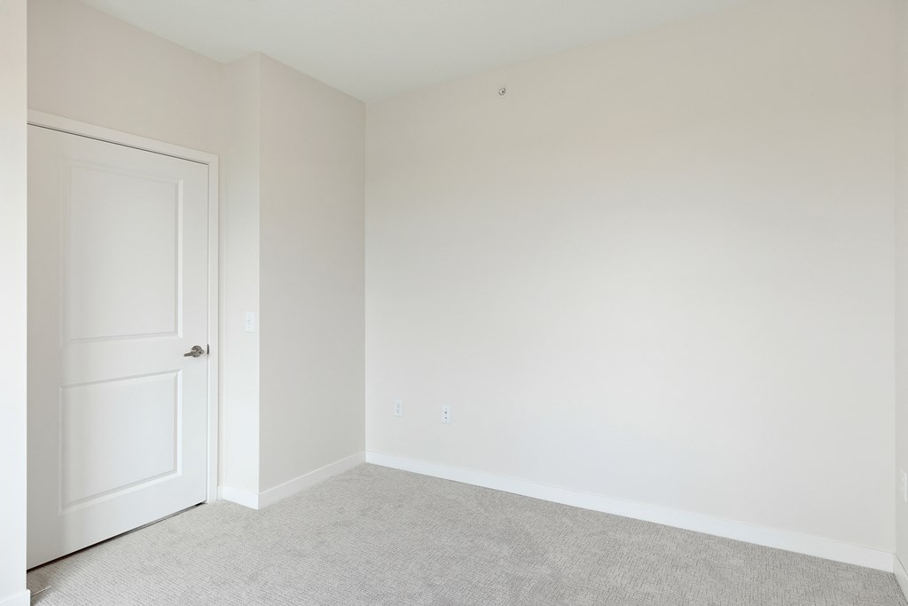 A white door is on the left of a room with white walls and carpeted floor at Sonder Point 50+ Apartments, Minnesota, 55430