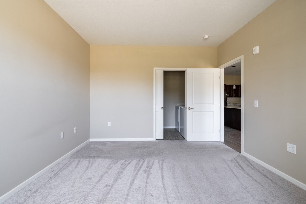 a bedroom with a carpeted floor and a door that leads to a kitchen
