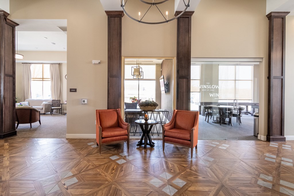 a lobby with two orange chairs and a table with a vase of flowers on it