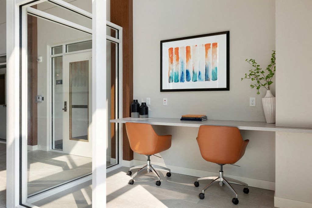 a home office with a desk and two orange chairs
