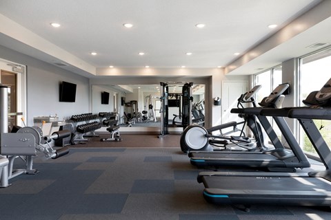 a gym with treadmills and other exercise equipment in a building with windows