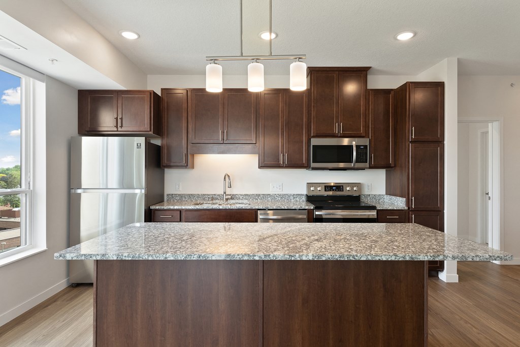 A kitchen with brown cabinets and a granite countertop at Sonder Point 50+ Apartments, Brooklyn Center, Minnesota
