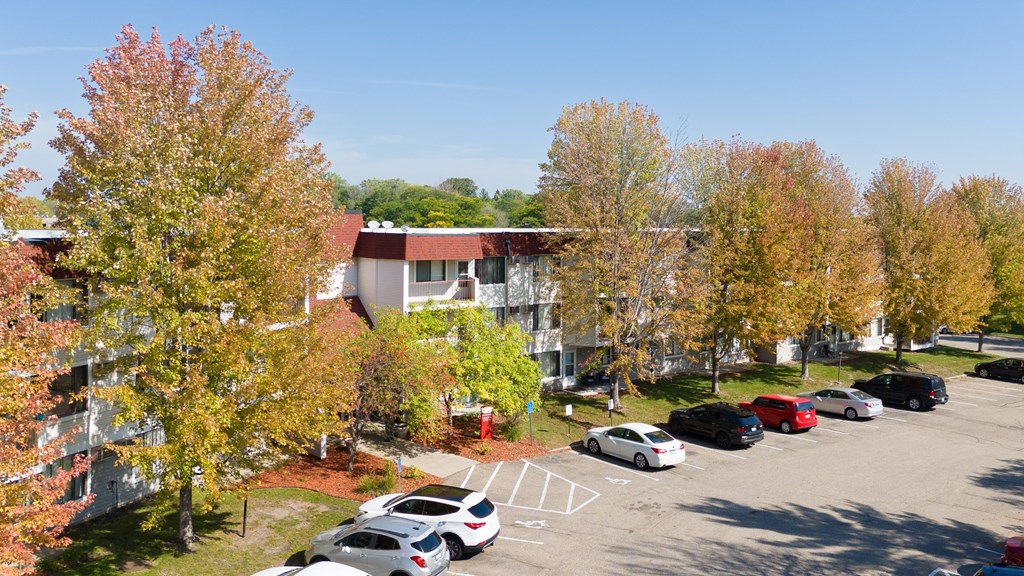 an aerial view of an apartment building with a parking lot and trees