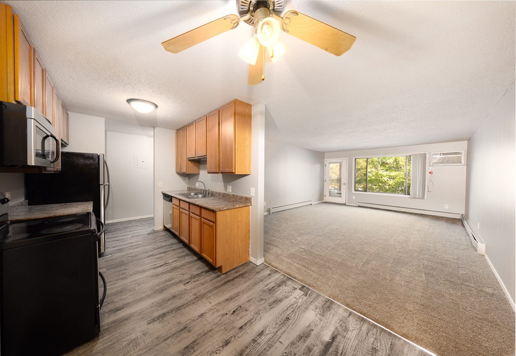 an empty living room with a kitchen and a ceiling fan
