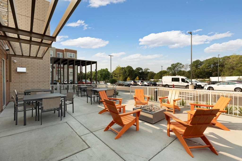 a patio with orange chairs and tables and a parking lot with cars