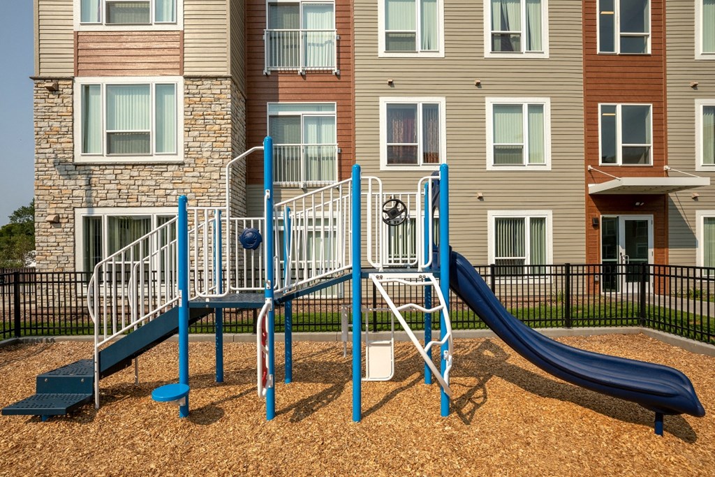 a playground with a blue slide in front of an apartment building