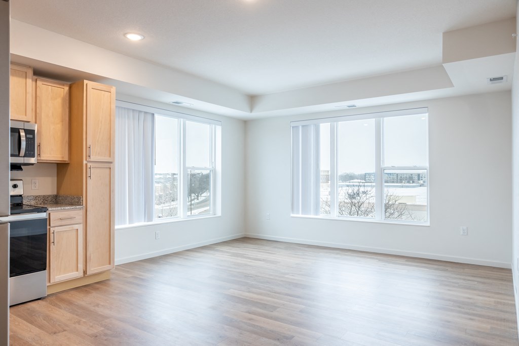 an empty living room and kitchen with wood flooring and large windows