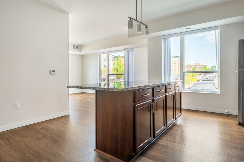 a kitchen and living room in an apartment with hardwood floors and a large window at Sonder Point 50+ Apartments, Brooklyn Center, MN, 55430