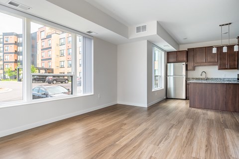 an empty living room with a large window and a kitchen in the background at Sonder Point 50+ Apartments, Brooklyn Center, 55430