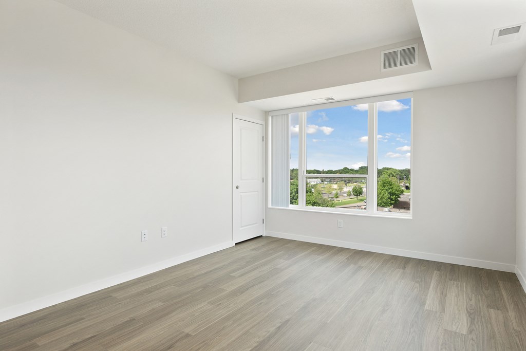 A room with a white door and a window showing a view of a residential area at Sonder Point 50+ Apartments, Brooklyn Center