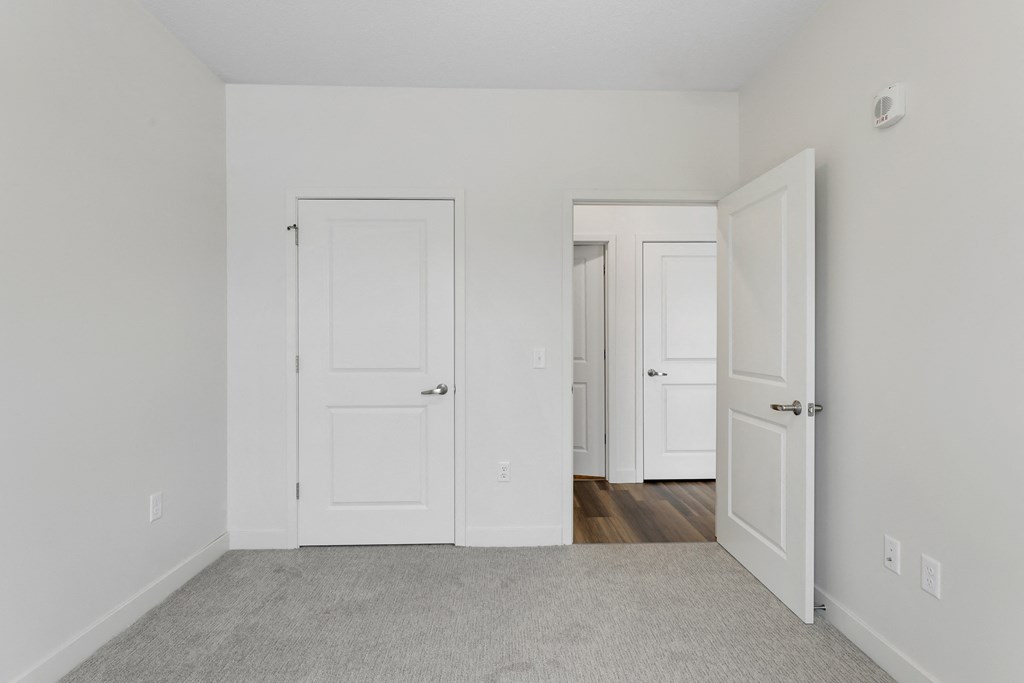 an empty bedroom with white doors and a carpeted floor