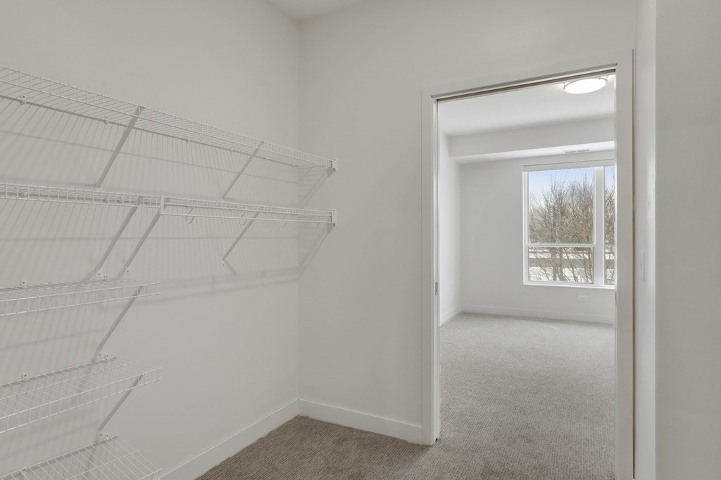 an empty room with a closet and a window and a white closet with metal shelves