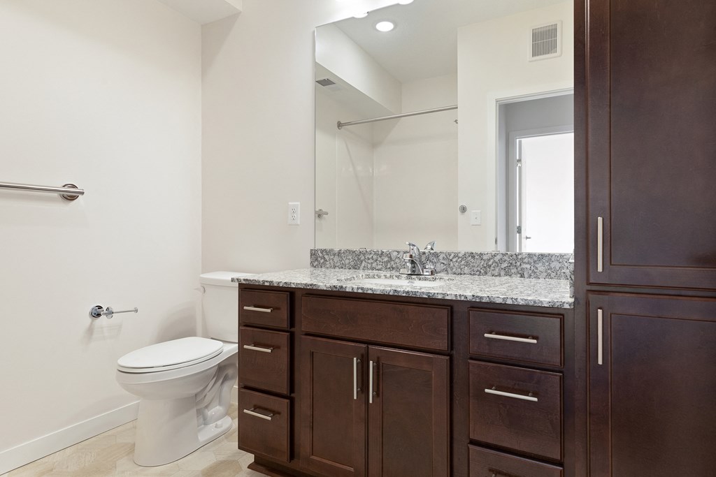 A white toilet sits in a bathroom with brown cabinets at Sonder Point 50+ Apartments, Brooklyn Center, 55430