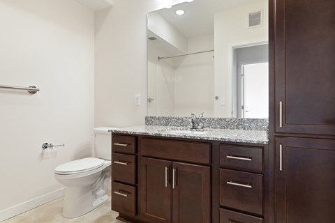 A white toilet sits in a bathroom with brown cabinets at Sonder Point 50+ Apartments, Brooklyn Center, 55430