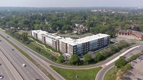 A large building with a white roof is surrounded by trees and a highway.
