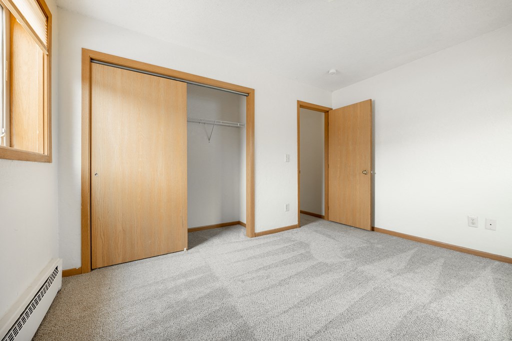 a bedroom with a carpeted floor and two closet doors at Ames Lake Neighborhood Apartments, St. Paul, MN, 55106