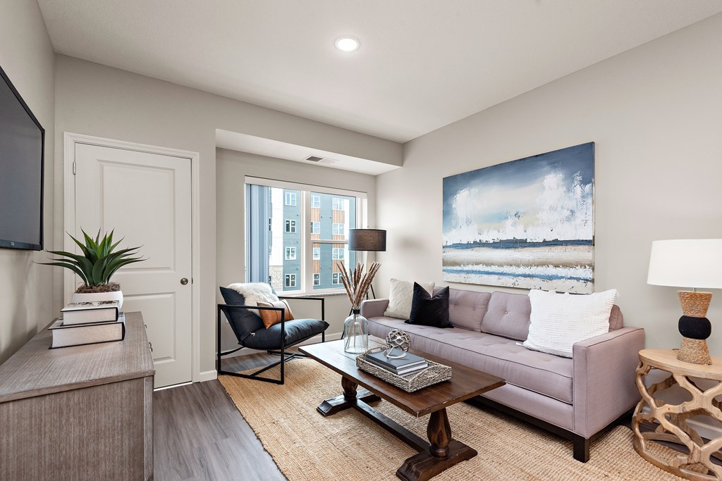 A living room with a grey couch, a coffee table, a chair, a potted plant, and a painting on the wall.