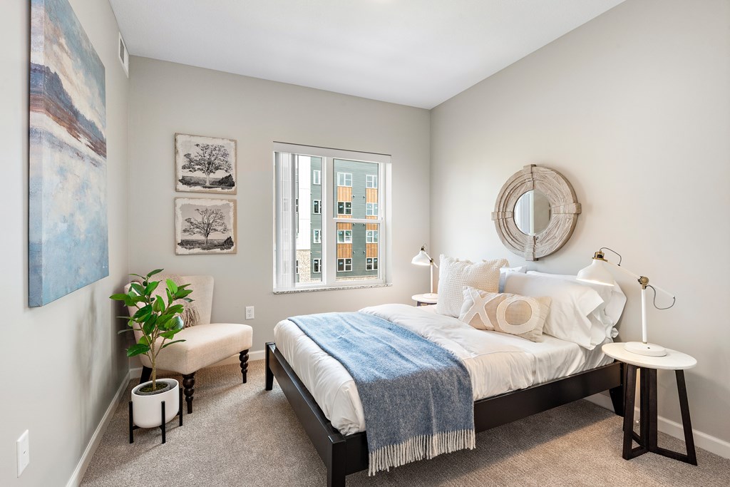 A bedroom with a bed, a bench, a side table, and a window.