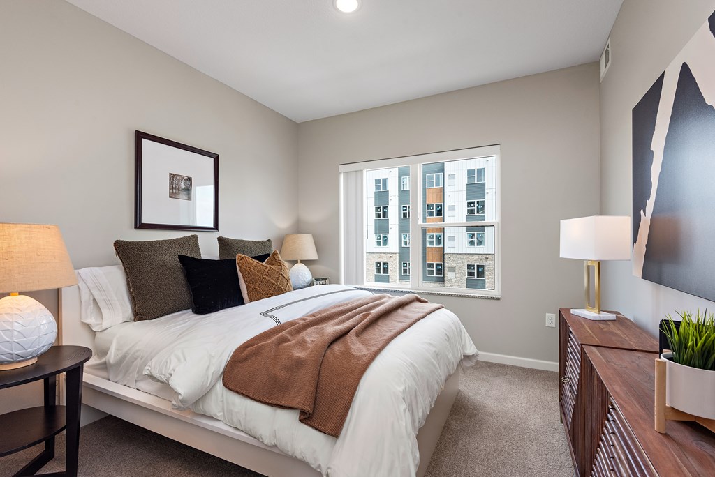 A bedroom with a large bed and a window showing a cityscape.