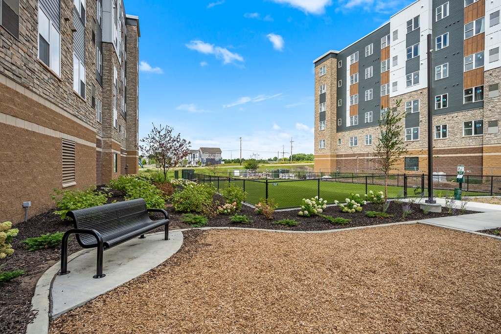 A black bench sits in a landscaped area between two apartment buildings.