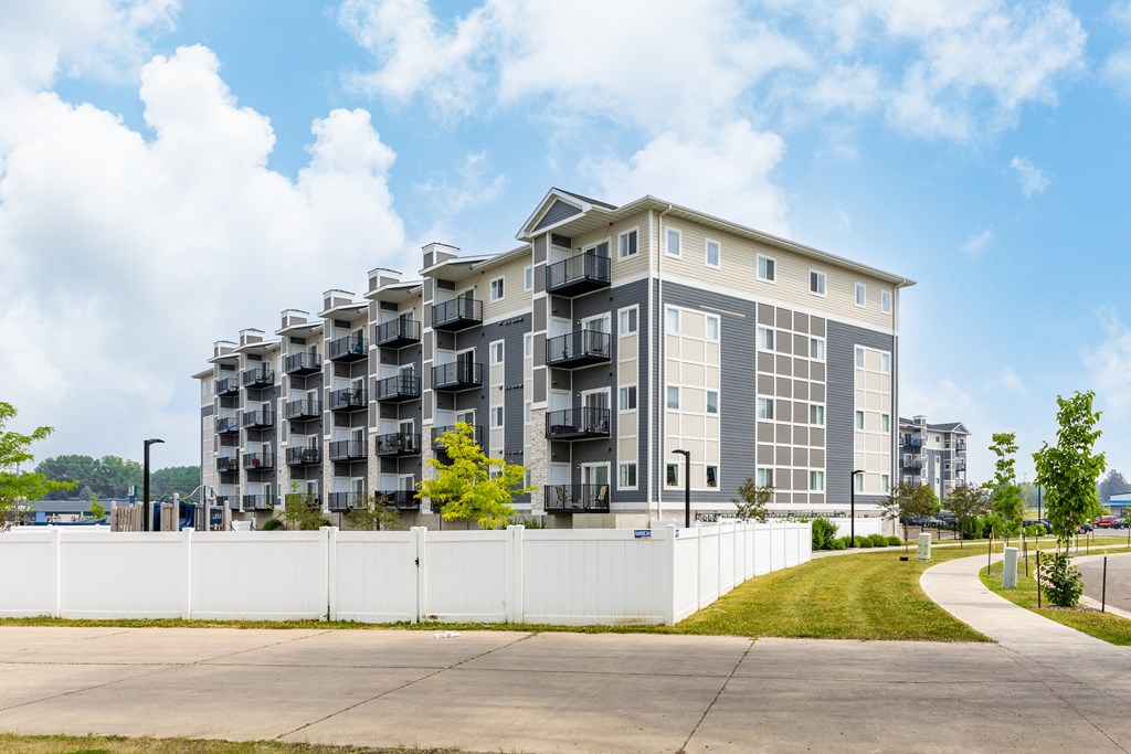 a grey apartment building with balconies and a white fence in front of it