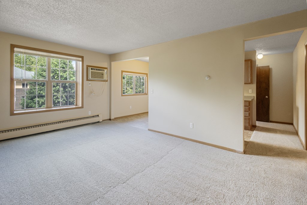 A spacious room with a carpeted floor and a door on the right side at Ames Lake Neighborhood Apartments, St Paul, MN