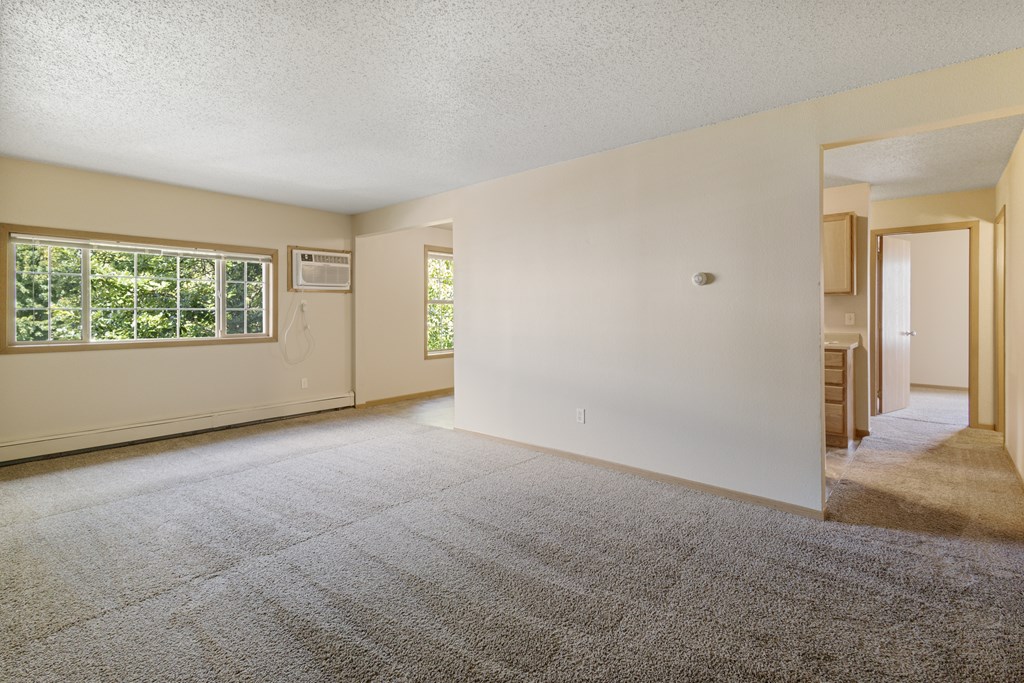 A large empty room with a carpeted floor and a window at Ames Lake Neighborhood Apartments, St Paul