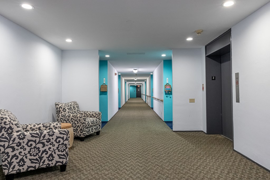 a long hallway with white and blue walls and a carpeted floor and some chairs at Humboldt Senior 55+ Apartments, Saint Paul, 55107