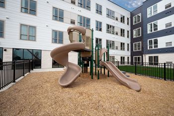 a playground with two slides and a chair in front of an apartment building at The Landing at Amber Fields Apartments, Rosemount, 55068