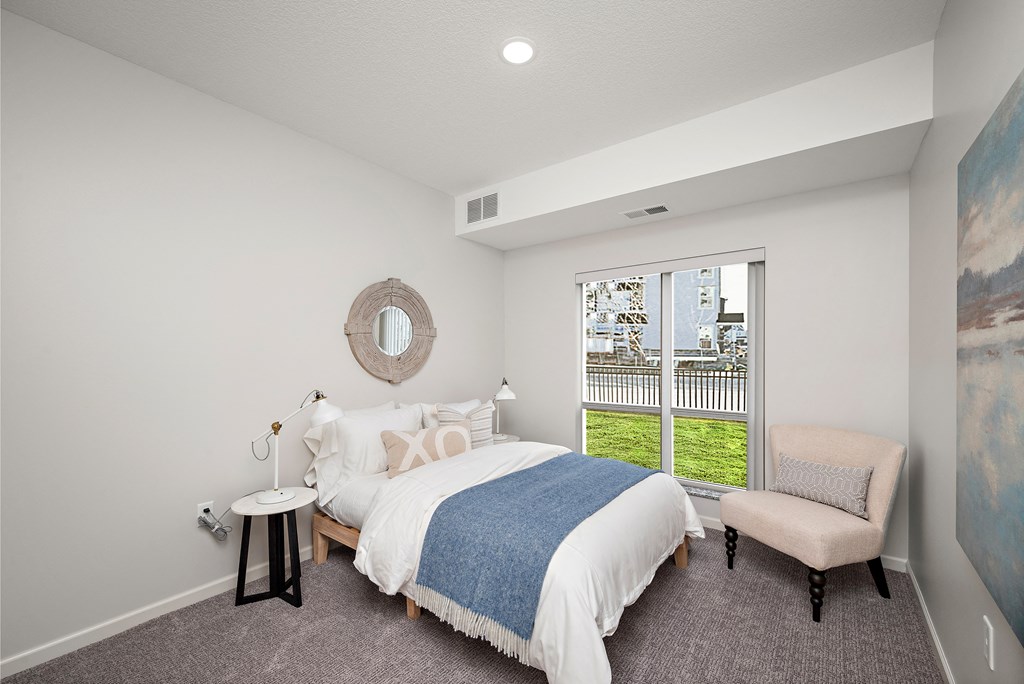 A bedroom with a large bed and a chair. at The Landing at Amber Fields Apartments, Rosemount