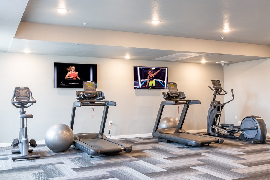 two treadmills and exercise balls in a gym with televisions at Technology Park Apartments, Minnesota