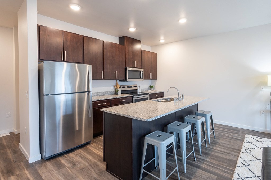 a kitchen with a large island with bar stools and stainless steel refrigerator at Technology Park Apartments, Rochester, MN