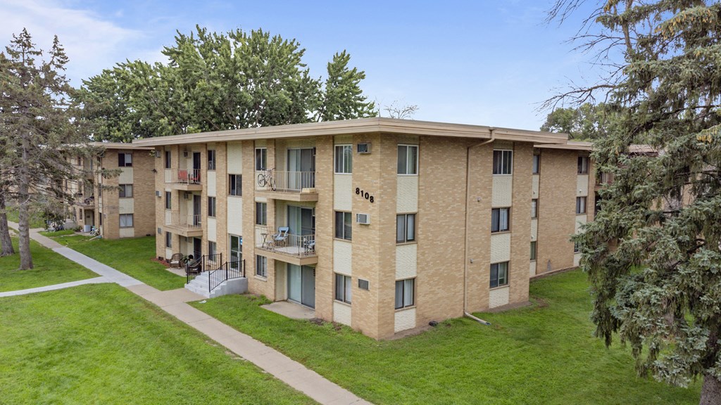 a brick apartment building with a green lawn and trees at Villa Del Coronado Apartments, Brooklyn Park, 55443
