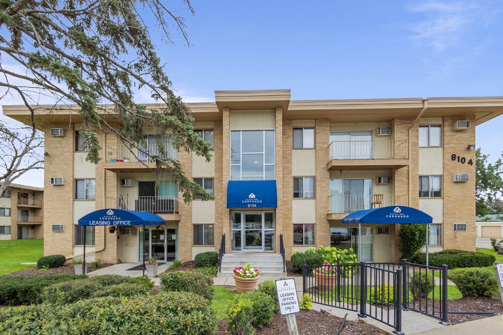 an apartment building with umbrellas and a sign in front at Villa Del Coronado Apartments, Brooklyn Park, MN, 55443
