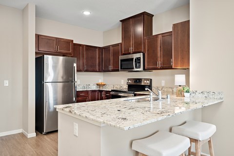 A kitchen with a granite countertop and white stools at The Winslow 62+ Apartments, West St Paul