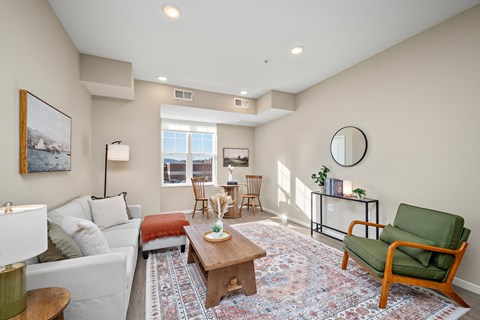 A living room with a white couch, a green chair, and a rug at The Winslow 62+ Apartments, West St Paul