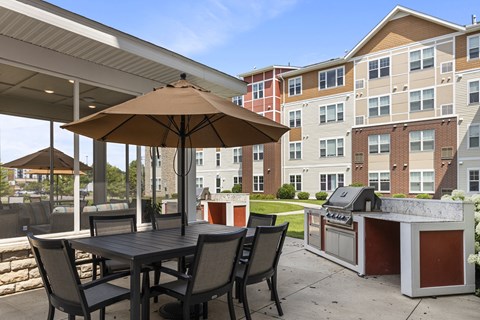 a patio with an umbrella and a table with chairs and a grill at The Winslow 62+ Apartments, Minnesota