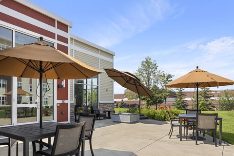 a patio with tables and umbrellas in front of a building at The Winslow 62+ Apartments, West St Paul, MN, 55118
