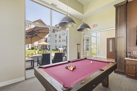 a pool table in a clubhouse with two lights hanging over it at The Winslow 62+ Apartments, West St Paul, Minnesota