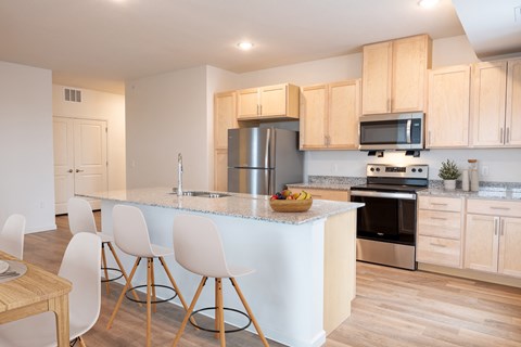 a kitchen with a large island with white chairs and a counter top