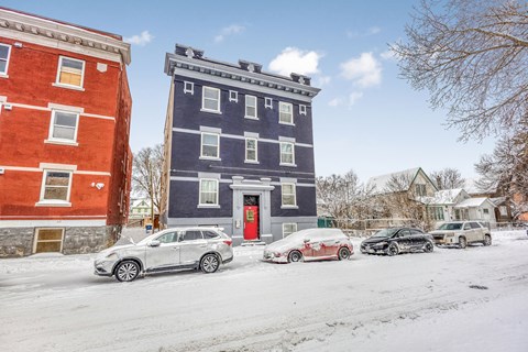 Cars are parked in front of a blue building with a red door.