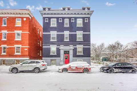 A red car is parked in front of a blue building.