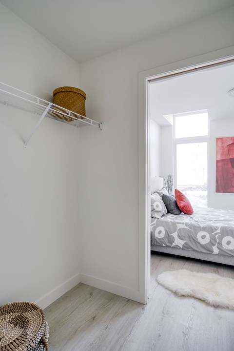 A white bedroom with a bed and a basket on the shelf.