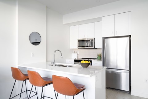 A modern kitchen with orange chairs and a white counter.